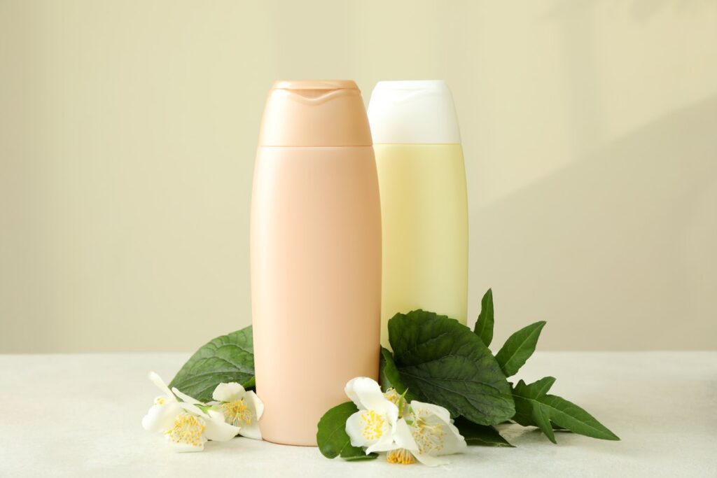 Dos botellas de champú suave sin etiqueta junto a flores blancas