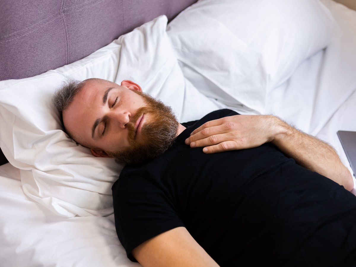 Hombre con barba y entradas durmiendo boca arriba con la cabeza apoyada en la almohada