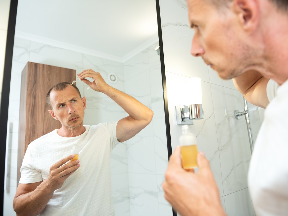 Hombre aplicándose una loción con cuentagotas en la línea del pelo frente al espejo del baño