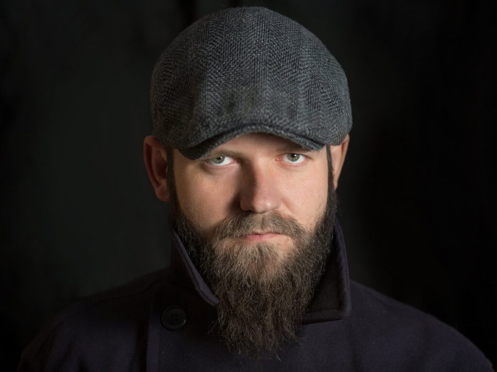 Hombre con barba y una gorra plana de tejido gris puesta sobre la cabeza