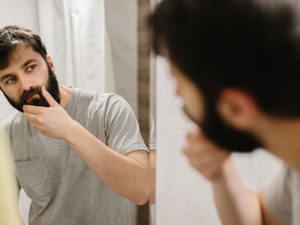 Hombre revisándose la barba con la mano frente al espejo del baño