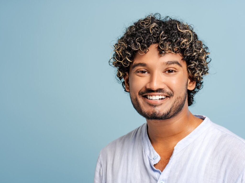 Hombre joven con el pelo rizado sonriendo sobre fondo azul claro
