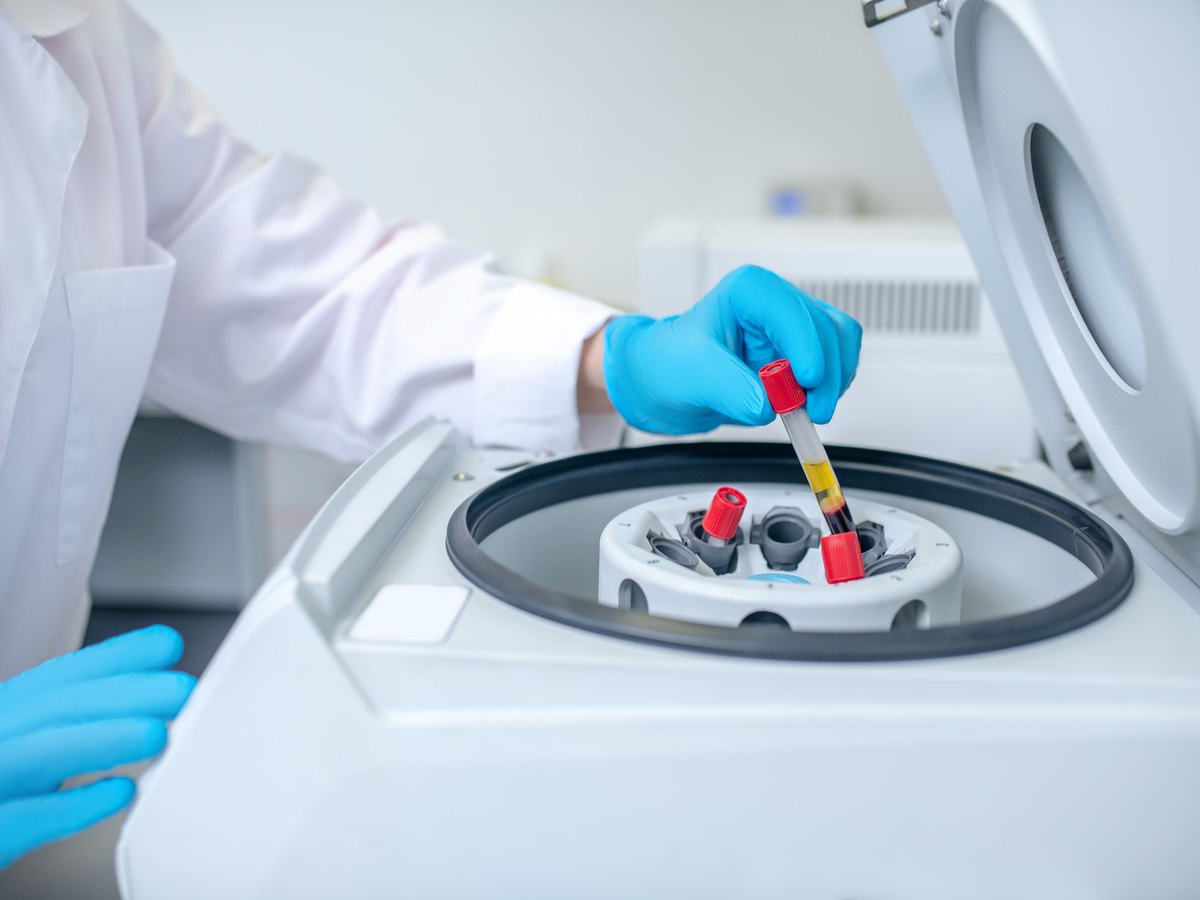 Profesional con bata y guantes colocando un tubo de muestra en una centrífuga de laboratorio